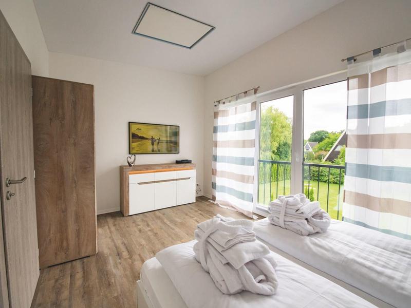 Bright hotel room with double bed, curtains, and green view outside the window.