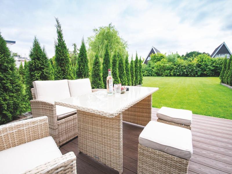 Cozy seating area with rattan chairs and table on a wooden deck overlooking the garden.