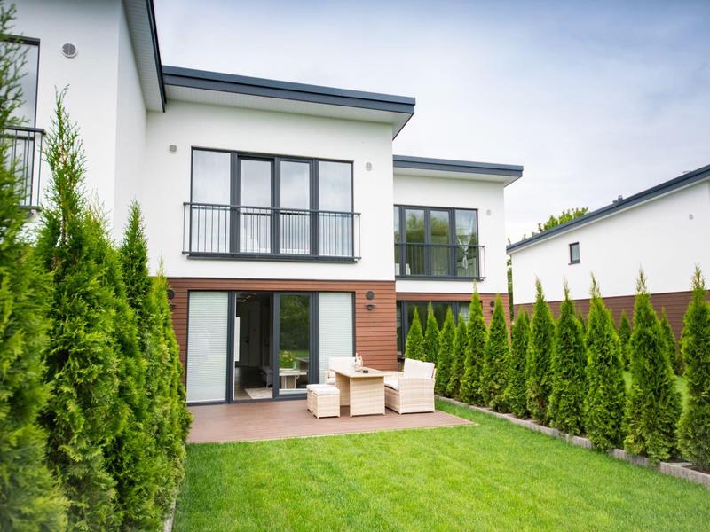 Modern two-story house with terrace and neat garden, surrounded by thuja hedges.