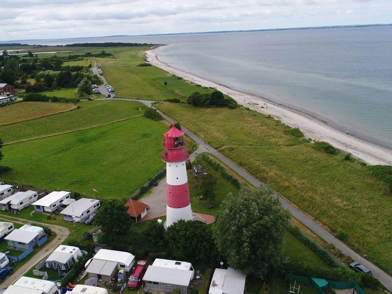 Red and white lighthouse on coast with beach, meadows, and RV park.