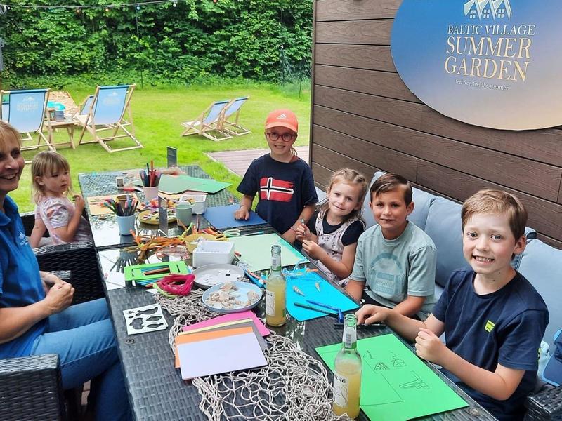 Group of children and an adult sitting outdoors with craft supplies on a table.