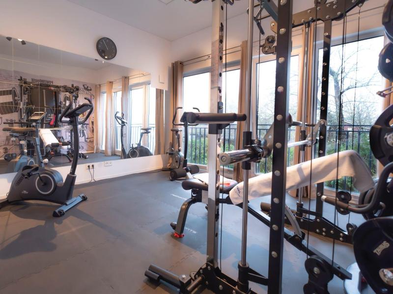 Modern gym with exercise equipment and large windows letting in daylight.