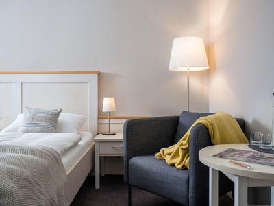 Modern hotel room with cozy bed, armchair with yellow blanket, and nightstand with lamp.