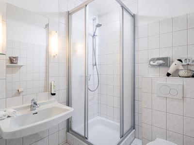 Compact white tiled bathroom with shower, sink, and toilet.
