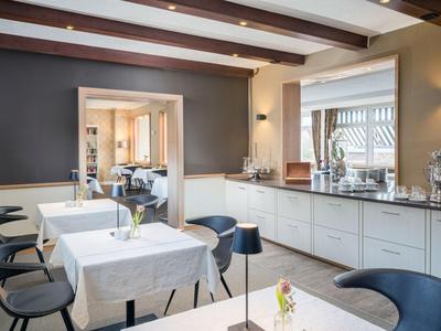 Moderner Frühstücksraum mit weißen Tischen und schwarzen Stühlen, hell und einladend gestaltet.