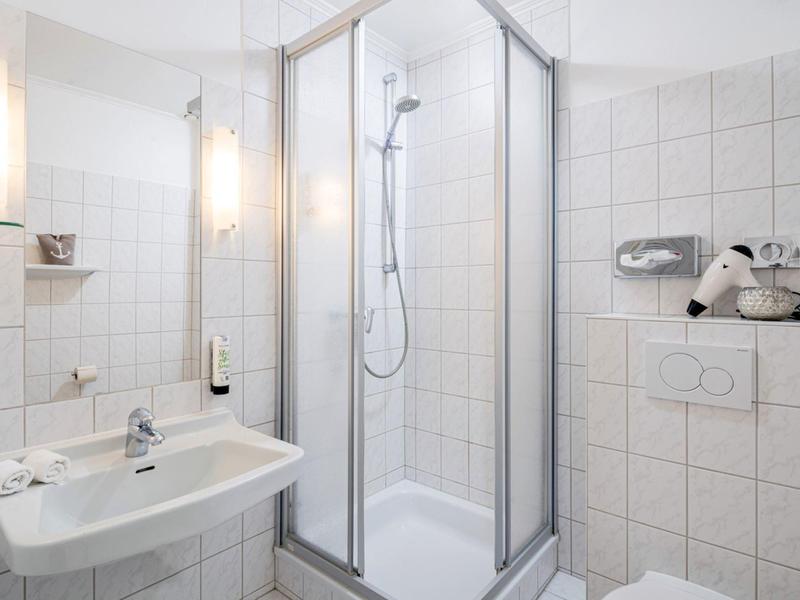 Compact white tiled bathroom with shower, sink, and toilet.