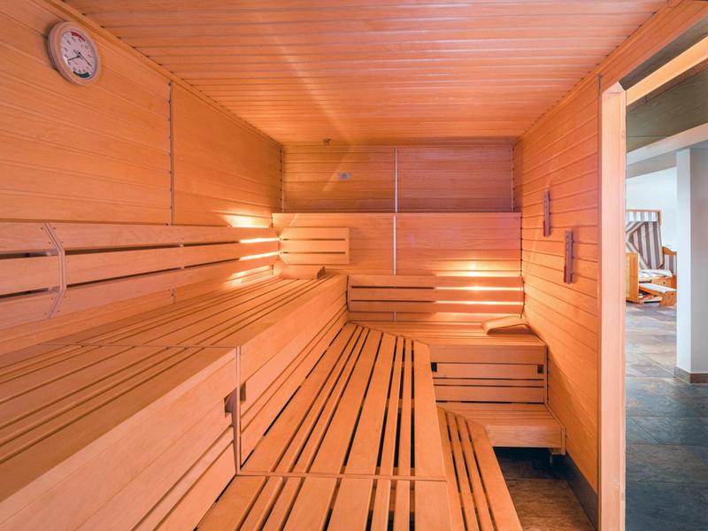 Bright wooden sauna with multiple seating levels and a wall-mounted thermometer.