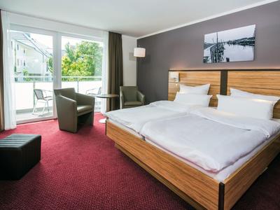 Modern eingerichtetes Hotelzimmer mit großem Bett, Balkon und rotem Teppich.