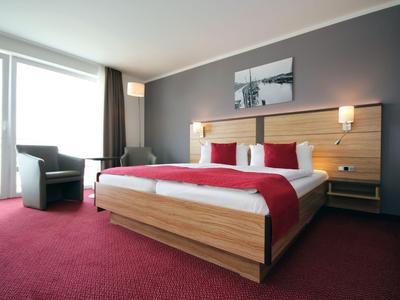 Modernes Hotelzimmer mit Doppelbett, roten Akzenten und Balkon mit Sitzmöbeln.