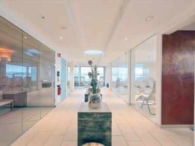 Moderner Hotelgang mit Glaswänden, Pflanzen und Sitzgelegenheiten, helle Beleuchtung