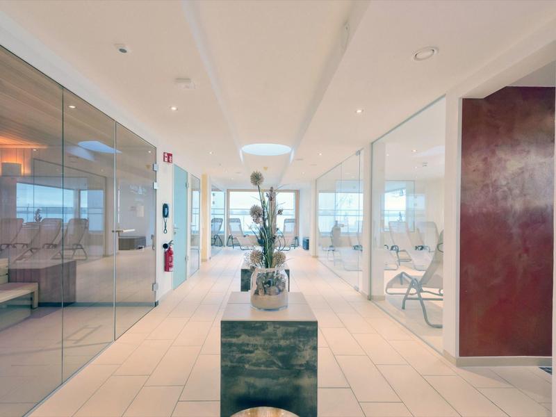 Jasny, nowoczesny korytarz hotelowy ze szklanymi ścianami i dekoracją kwiatową pośrodku.