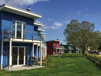 Mehrere bunte Ferienhäuser liegen an einem grasbewachsenen Hang unter blauem Himmel.