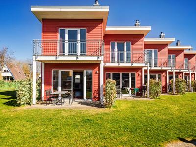 Mehrere zweistöckige, rote Ferienhäuser mit Balkonen und Terrassen vor einem grünen Rasen.