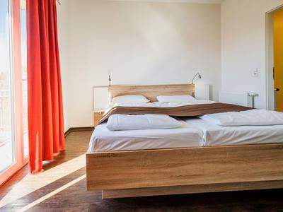 Schlafzimmer mit großem Bett, Holzrahmen, weißen Bettwaren und roten Vorhängen neben großem Fenster.