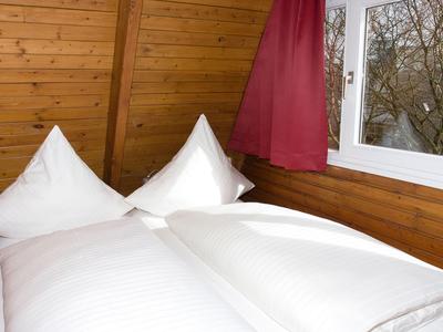 Gemütliches Bett mit weißen Bettwäsche und Holzwänden in einem Hotelzimmer mit Fenster.