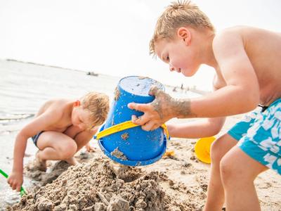 Zwei Jungen bauen am Strand mit Eimern Sandburgen nahe dem Wasser.