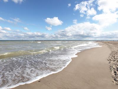 Weitläufiger Sandstrand mit sanften Wellen und blauem Himmel mit Wolken.