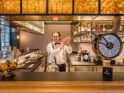 Barkeeper in moderner Bar schüttelt Cocktail mit Barutensilien und Früchten.