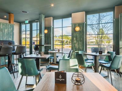 Modern eingerichteter Frühstücksraum mit grünen Stühlen und großen Fenstern mit Blick auf den Garten.