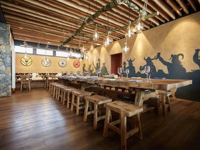 Rustikaler Gastraum mit Holztischen, Bänken, Balkendecke und großer Wandmalerei