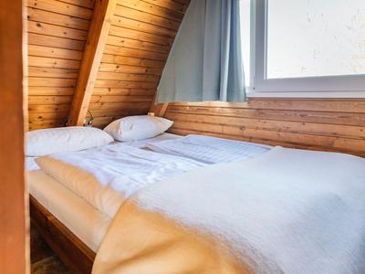 Gemütliches Schlafzimmer mit Holzwänden, Bett mit weißen Decken nahe einem großen Fenster.