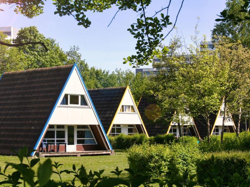 Drei dreieckige Ferienhäuser in einer grünen Parkanlage an einem sonnigen Tag.