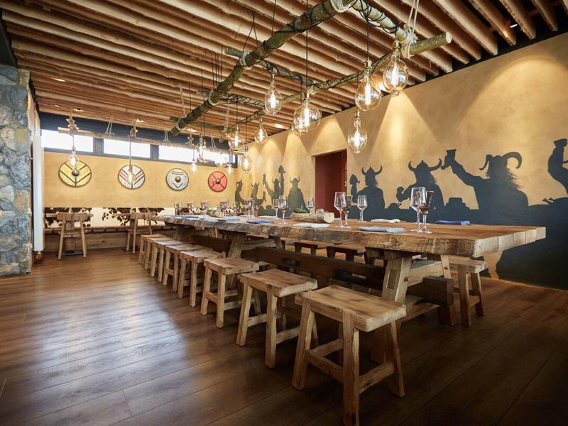 Rustikaler Gastraum mit Holztischen, Bänken, Balkendecke und großer Wandmalerei