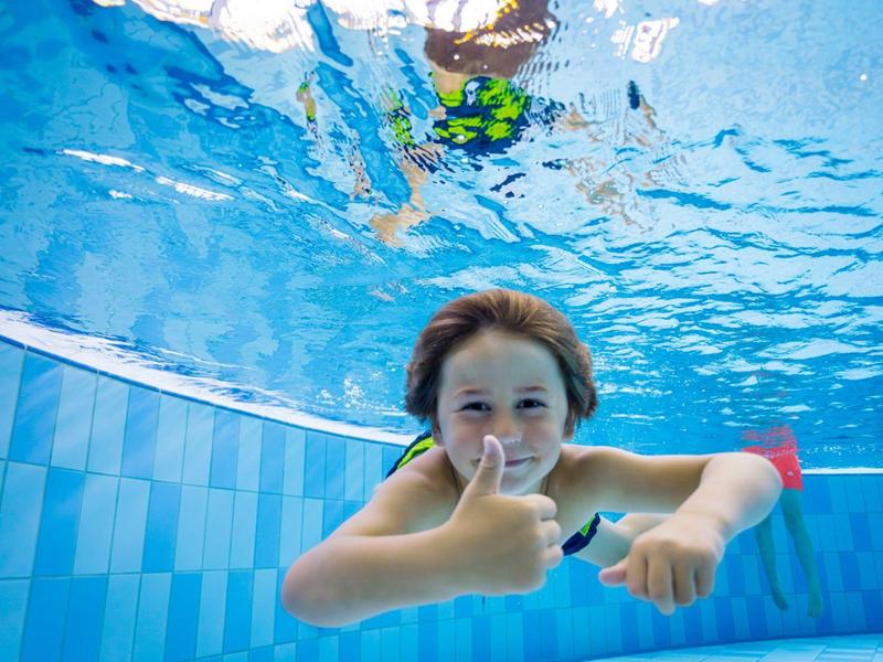 Kind taucht im Pool und zeigt Daumen hoch unter Wasser