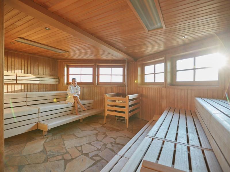 Holzsauna mit Steinboden, Holzliegen und einer entspannenden Person.