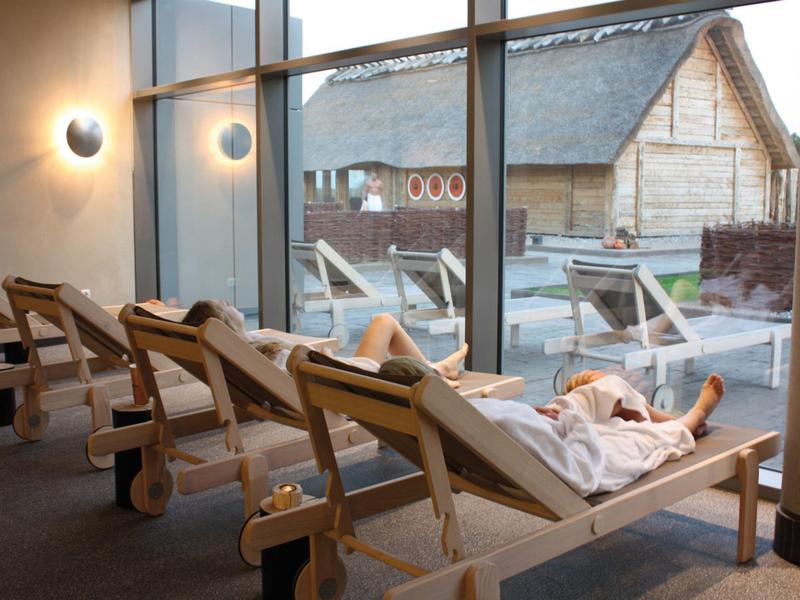 Person entspannt auf Liegestuhl mit Blick auf Außenbereich und Holzhütte.