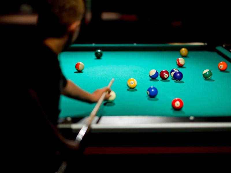 Person spielt Billard an einem grünen Tisch mit mehreren bunten Kugeln.