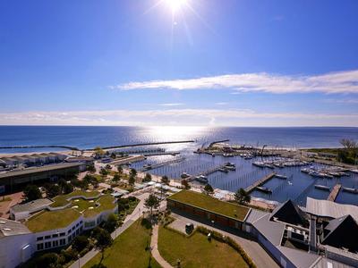 Pohled na marínu s loděmi, pláží a jasnou oblohou za slunečného počasí.