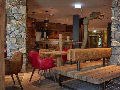 Gemütlicher Hotel-Loungebereich mit Stühlen, Tischen und rustikaler Steinwand.