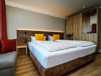 Modernes Hotelzimmer mit Doppelbett, Holzdesign und bunten Kissen.