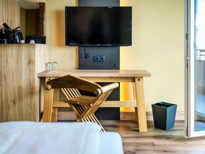 Moderner Hotelzimmerbereich mit Holzarbeit, TV an der Wand und Balkonzugang.