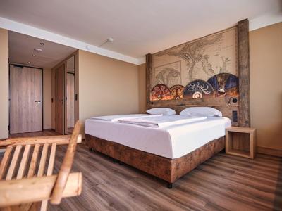Modern eingerichtetes Hotelzimmer mit Doppelbett, Holzmöbeln und Wandkunst im warmen Farbton.