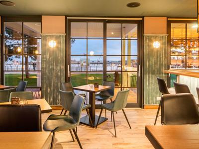 Moderner Hotelrestaurant-Innenraum mit Blick auf Wasser und Sitzbereichen bei Sonnenuntergang.