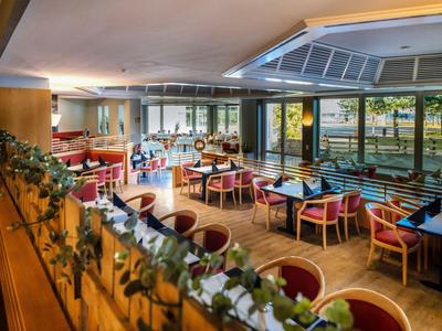 Helles Restaurant mit modernen Holzmöbeln und Panoramafenstern neben einem Schwimmbad.