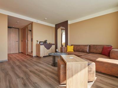 Moderní hotelový pokoj s hnědým gaučem, dřevěnou podlahou a minimalistickým zařízením.