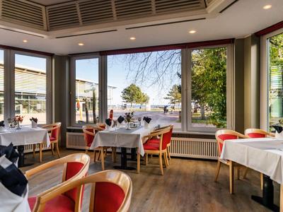 Helles Restaurant mit Holzboden, roten Stühlen und großen Fenstern mit Blick auf die Straße.