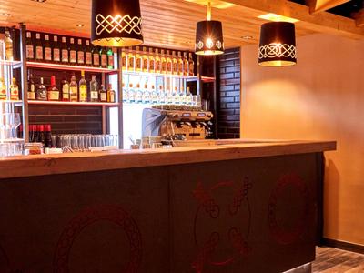 Moderne Hotelbar mit Holzdecke, Sessel, Barhockern und beleuchtetem Regal voller Getränke.