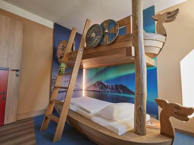 Dětská palanda ve tvaru lodi s dřevěným žebříkem před barevnou stěnou v hotelovém pokoji