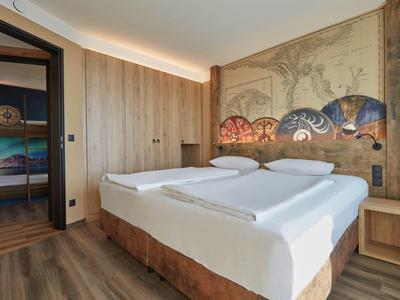 Moderní hotelový pokoj s manželskou postelí, dřevěnou podlahou a zdí s uměleckou výzdobou.