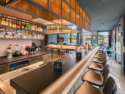 Modern hotel bar with black stools, long counters, and large windows.