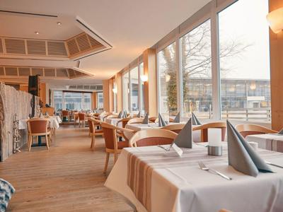 Bright restaurant with wooden floor, tables with white cloths, and large windows overlooking outside.