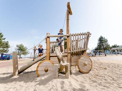 Kind spielt auf hölzernem Piratenschiff-Spielplatz im Sand mit klarem Himmel.
