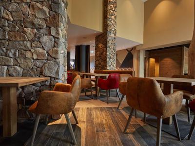 Innenraum einer gemütlichen Hotelbar mit braunen Sesseln und Steinsäulen.