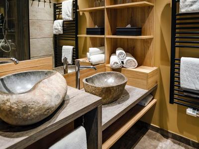 Modernes Badezimmer mit zwei naturstein Waschbecken und Holzregalen voller Handtücher.