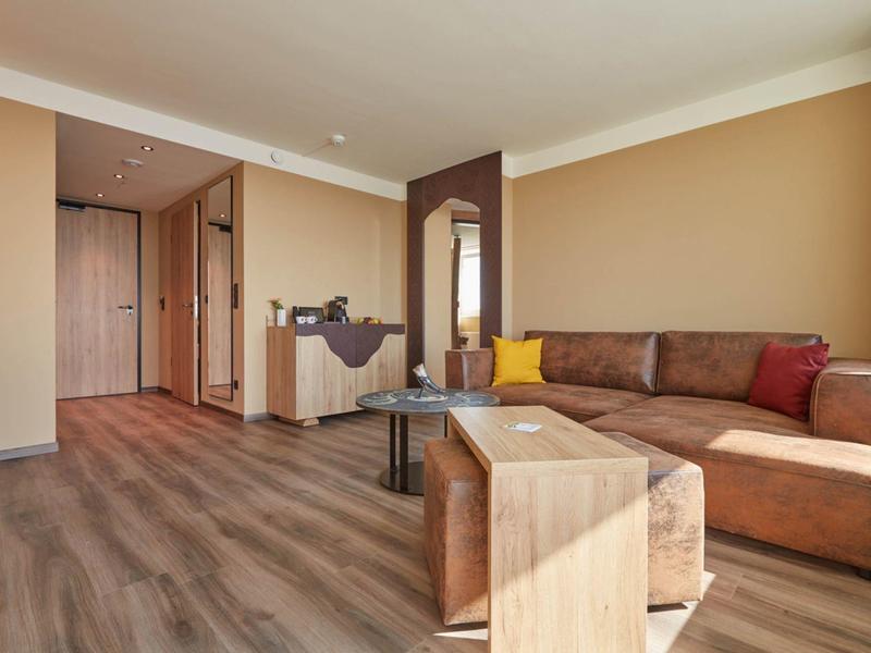 Moderní hotelový pokoj s hnědým gaučem, dřevěnou podlahou a minimalistickým zařízením.