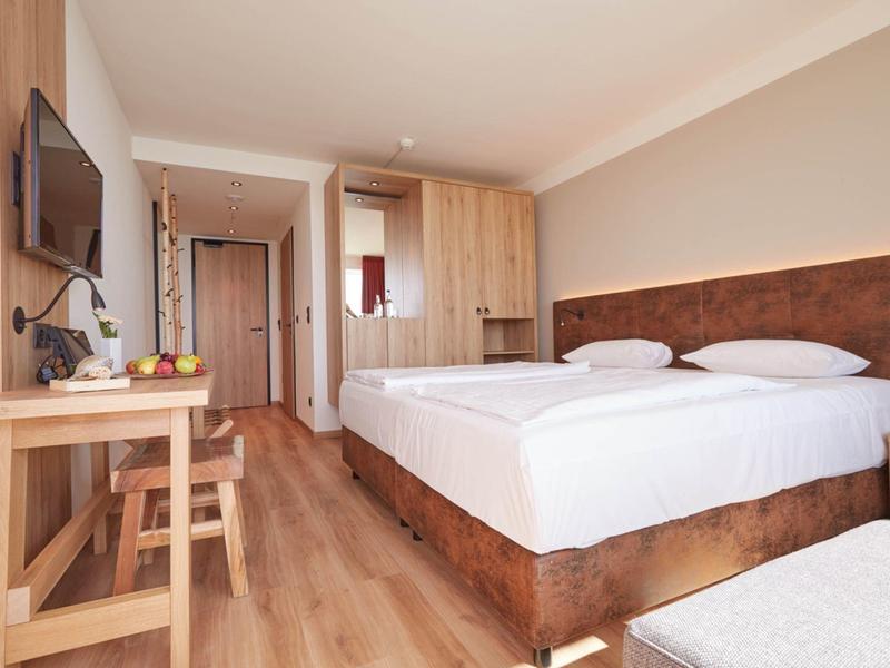 Moderní hotelový pokoj se dvěma postelemi, dřevěným nábytkem a psacím stolem se židlí.